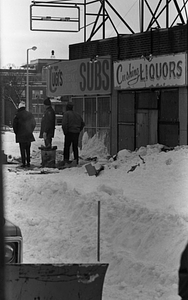 Unidentified men warming themselves by fire in trash can alongside snowdrifts