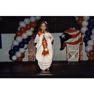 A girl holds up her white dress while she speaks into a microphone at the Festival Puertorriqueño