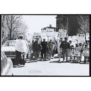 Children holding up their signs and walking down the street as a woman with a toddler looks on during the Boys and Girls Clubs of Boston 100th Anniversary Celebration Parade