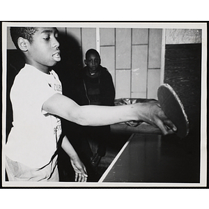 A boy plays table tennis as another boy looks on