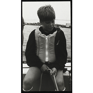 A boys holds a rope as he sits on the deck of a sailboat in Boston Harbor