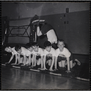 A boy jumps head first into six boys on their hands and knees in the South Boston gymnasium on Physical Fitness Day