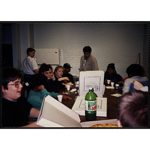 A group of children and site coordinator Josh Kraft gather around a table with pizza at the Tri-Club youth leadership event at the South Boston Clubhouse