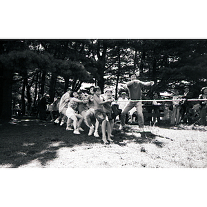 Children and young adults play tug-of-war in a wooded picnic area