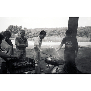 Men flip burgers on a grill, while a man and woman stand to the side