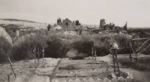 Eight wooden crosses marking graves, one with a helmet hung on it and a destroyed stone building in the background, Berry-au-Bac