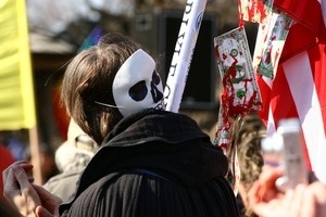 Protesters carrying an American flag hung with bloody dollar bills and wearing a skull mask: rally and march against the Iraq War