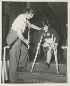 Boy walking down stairs with crutches and leg braces - Digital Commonwealth