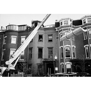 Workman watching from a window as a load of lumber swings towards the building at 326 Shawmut Avenue from a crane parked on the street below.