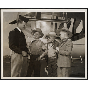 Three boys in cowboy garb pose with an unidentified pilot next to a plane