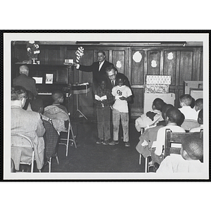 A man looks over the shoulders of two boys as they sing accompanied by piano before an audience at a Christmas event