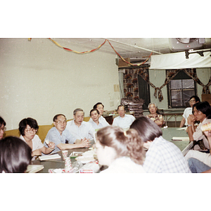 Henry Wong speaks while sitting at a table withto other Chinese Progressive Association members during a tutoring class dinner