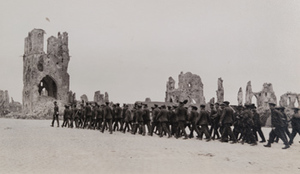 Group of British soldiers, some carrying shovels, marching past destroyed Cloth Hall, Ypres, 1919