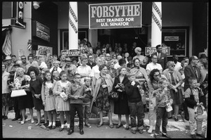 Crowd of children and families under a Forsythe for Senator banner, watching Robert F. Kennedy walk past during the Turkey Day festivities