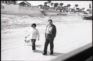 Middle-aged couple walking on beach with pet dog