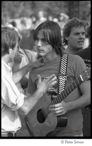 Jackson Browne, with acoustic guitar, talking to unidentified man at the No Nukes concert and protest, Washington, D.C.