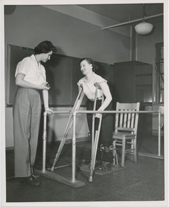 A client with crutches and leg braces practices getting up from a seated position