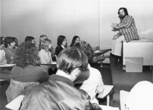Suffolk University Professor Malcolm Barach (CAS) seated on top of desk, lecturing to students in classroom