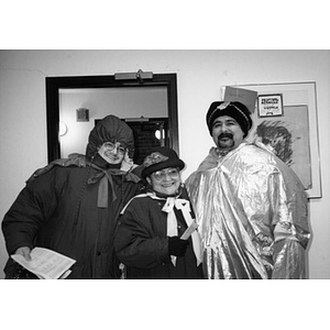 Man dressed as one of the Three Kings poses with two people dressed in winter coats and hats.