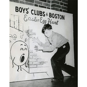 A boy poses next to an interactive Easter poster that reads "Boys' Clubs of Boston Easter Egg Hunt"