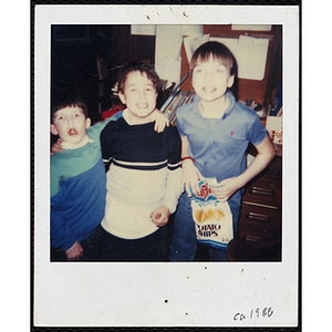 A boy with a bag of potato chips smiles for the camera while two other boys pose with their arms around each other at the Boysand Girls Club