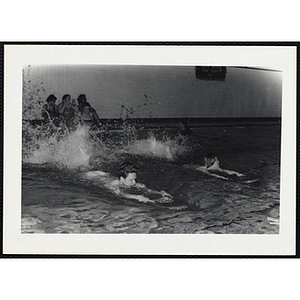 Two teenage boys swim with paddle boards in a natorium pool