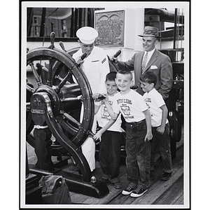 Three boys, Boston Rotary Club president Arthur Curren Jr. (rear), and seamen Edward Smith pose for a group shot at wheel of the USS Constitution