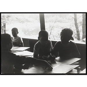 Four boys sit at a table with pencils and paper