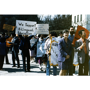 Demonstrators march with protest signs in front of the Massachusetts State House at a rally for bilingual education in schools