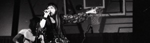 Unidentified band in performance in what appears to be a high school gymnasium: panoramic shot of violinist and guitarist