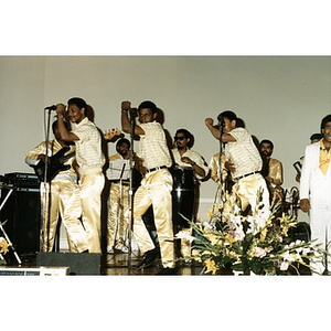 Young men in gold pants dancing, singing, and playing music on stage.