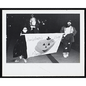Children in Halloween costumes march with a banner in a night parade