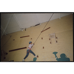 A child wearing a safety harness climbs a wall of a gymnasium