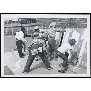 A group of boys apply white paint on large board during Tom Sawyer Day