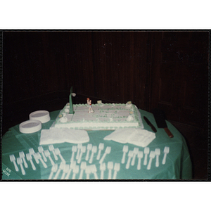 A table with a decorated cake commemorating a basketball season is set with plates, napkins, and forks
