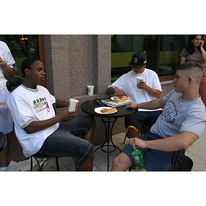 Three male Torch Scholars eat pizza during the Question and Answer Pizza Party