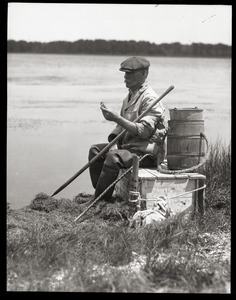 Otis Fish, the blind clam digger of Falmouth: portrait of Fish seated by the shore, wearing waders and holding a clam