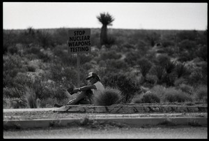 Activist seated by the road with a sign reading 'Stop nuclear weapons testing,' at the Nevada Test Site peace encampment