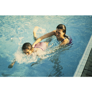 Adult helping child to swim in pool