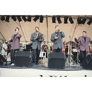 Four men stand at microphones on stage at the Festival Puertorriqueño