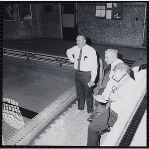 A man speaks into a microphone while two others look at a swimming pool during the Boys' Clubs of America New England Regional Swimming Championships at Harvard