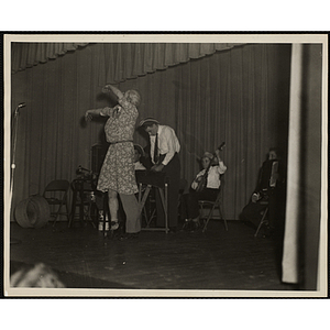 A man in drag dances on a stage as the Bunker Hillbillies play their instruments behind him