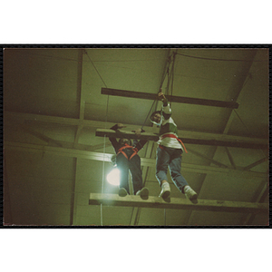 Two children stand on wood beams in a gymnasium