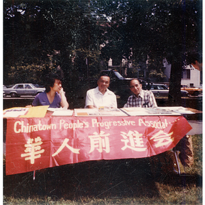 Three Chinese Progressive Association members sit at a Chinese Progressive Association table outside