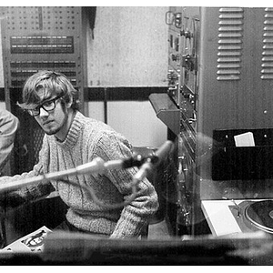 Young man seated at the turntable in the broadcast booth at the WNEU studio