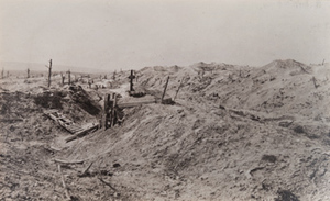 View of a dugout entrance and a cross standing amongst barren hillocks