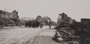 Soldiers walking along a cobblestone steet surrounded by destroyed stone buildings on both sides