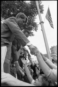 Robert F. Kennedy atop an outdoor stage, shaking hands with the crowd at the Turkey Day parade while stumping for Democratic candidates in the northern Midwest