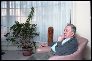 Fine art photographer Aaron Siskind: portrait with a potted plant in the background, while seated in a armchair in his living room