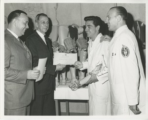 James Burrows presents a certificate of completion of training to a 1964 Prosthetics and Orthotics training graduate while two other men look on